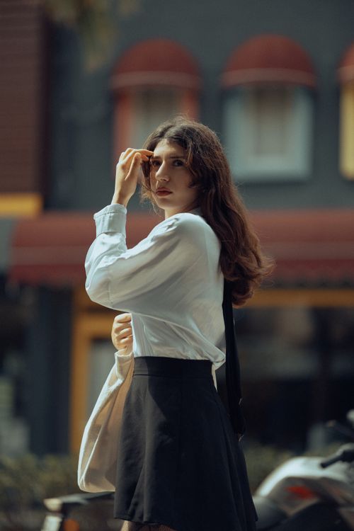 Free Fashionable young woman in white blouse and black skirt walking in the city, exuding confidence. Stock Photo