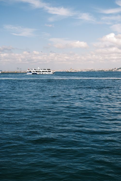 Free A ferry sails across a calm blue ocean under a partly cloudy sky, ideal for summer travel. Stock Photo