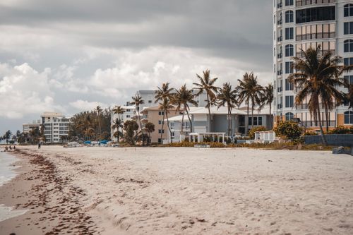 Free Beautiful resort on a sandy beach with palm trees under a cloudy sky, perfect for a summer vacation. Stock Photo