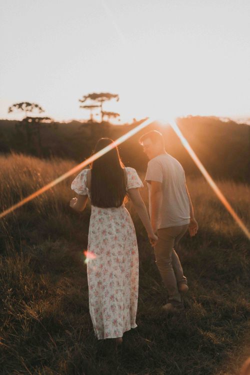 Free A young couple enjoying a romantic walk at sunset in a summer field, capturing love and serenity. Stock Photo