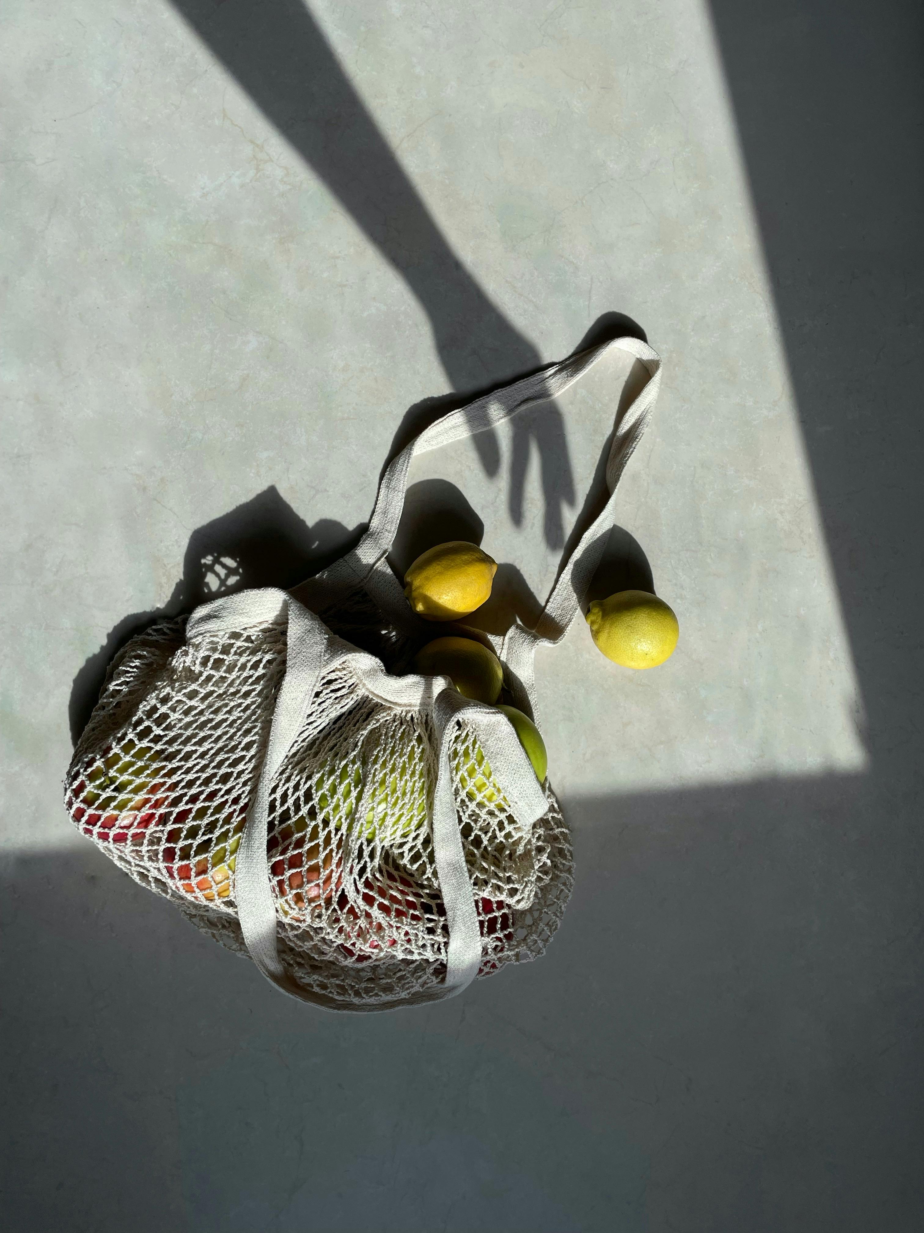 A mesh bag filled with lemons casts shadows in bright sunlight.