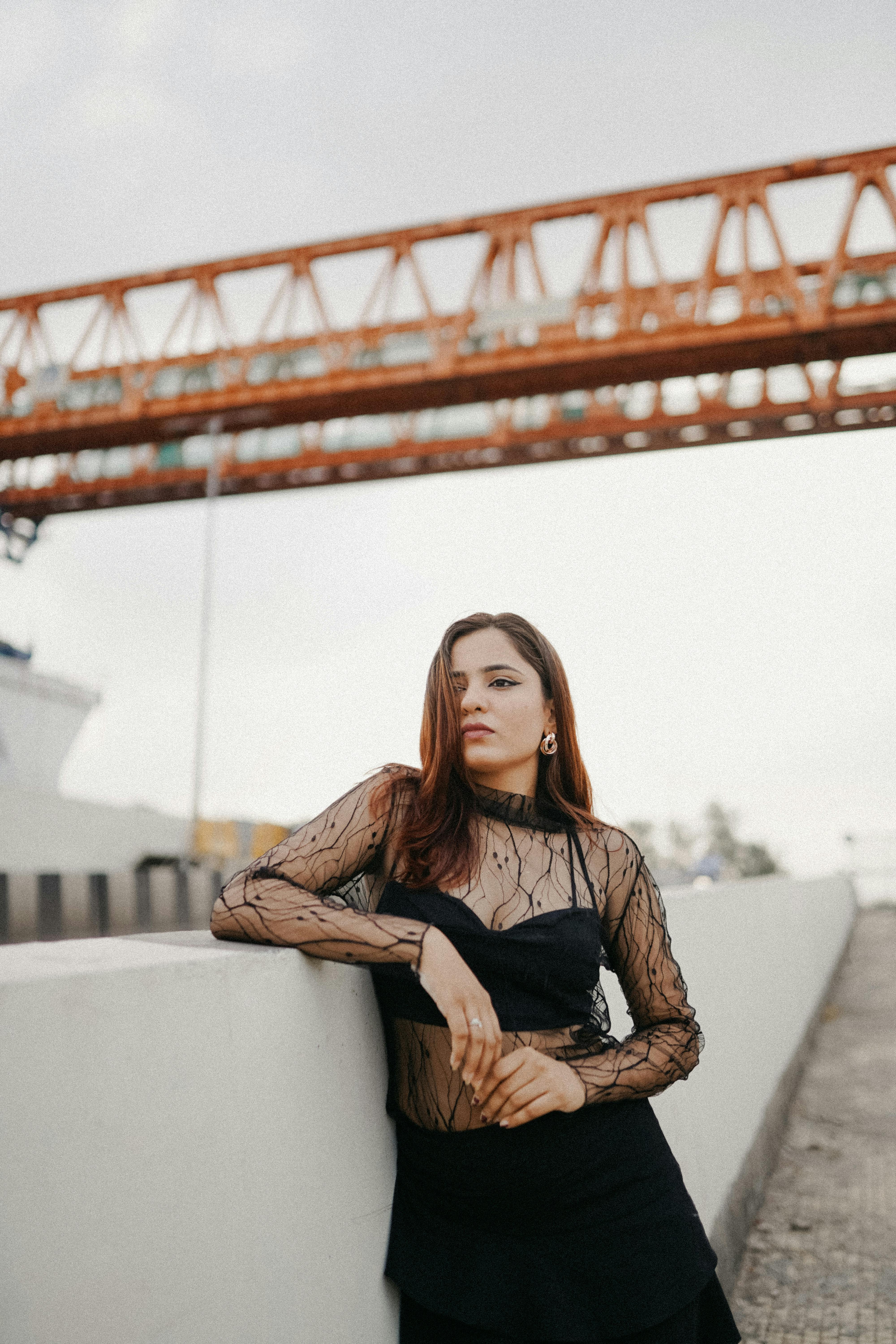 Stylish woman in a black outfit poses confidently on an urban bridge, showcasing modern fashion.