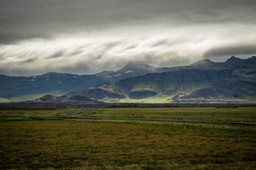 Free Scenic view of a dramatic mountainous landscape under stormy skies with lush grassland in the foreground. Stock Photo