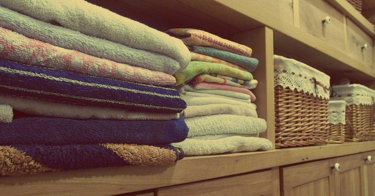 Como Organizar Roupa de Cama e Toalhas: Guia do Enxoval da Casa Armário de madeira com toalhas empilhadas e cestos decorativos