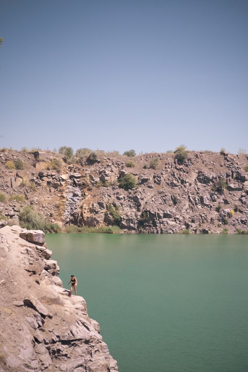 Free Person cliff jumping into a lake under clear summer skies, showcasing adventure and natural beauty. Stock Photo