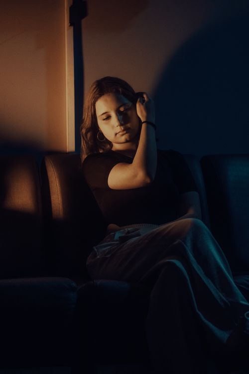 Free A thoughtful woman sits on a sofa in a dimly lit room, creating a moody atmosphere. Stock Photo