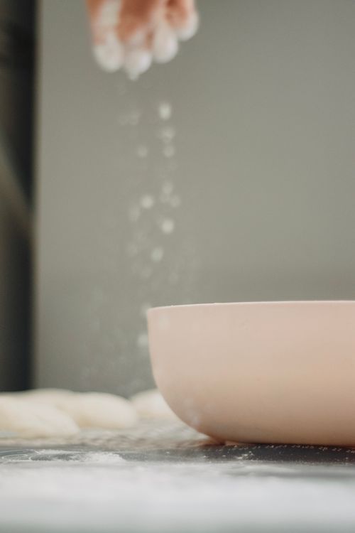 Free Close-up of dough preparation with flour sprinkling into bowl, creating indoor baking scene. Stock Photo