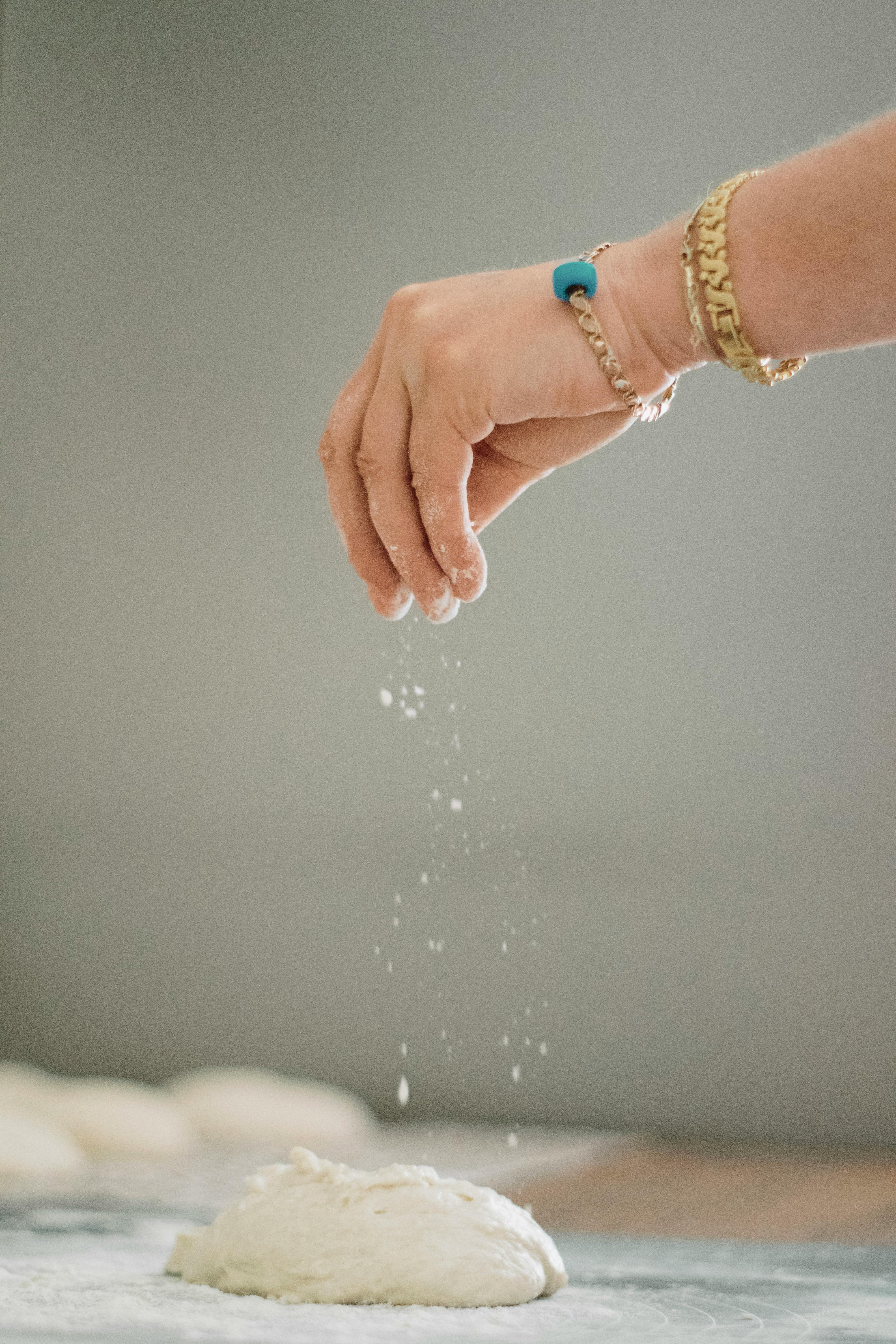 person hand adding flour to dough