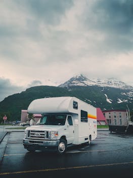 Camper van parked against a backdrop of majestic snow-capped mountains in a quiet, picturesque town.