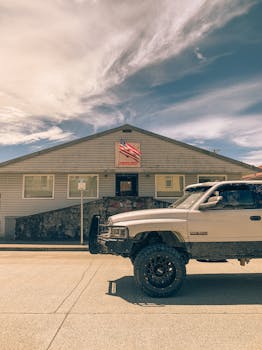 Vintage pickup truck parked in front of a small town building with a USA flag on a sunny day.
