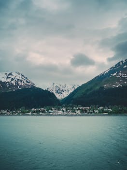 Charming coastal town nestled between snow-capped mountains under a cloudy sky, perfect for travel inspiration.
