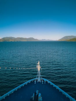 A cruise ship glides through Alaska's calm waters surrounded by scenic mountains on a sunny day.