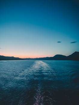 Serene ocean view at sunset with silhouetted mountains and vibrant sky.