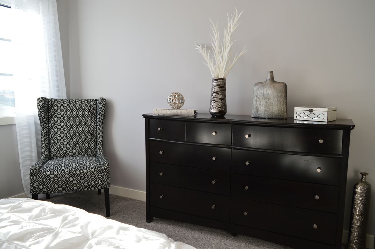 Black dresser with round knobs styled with vases beside a patterned chair