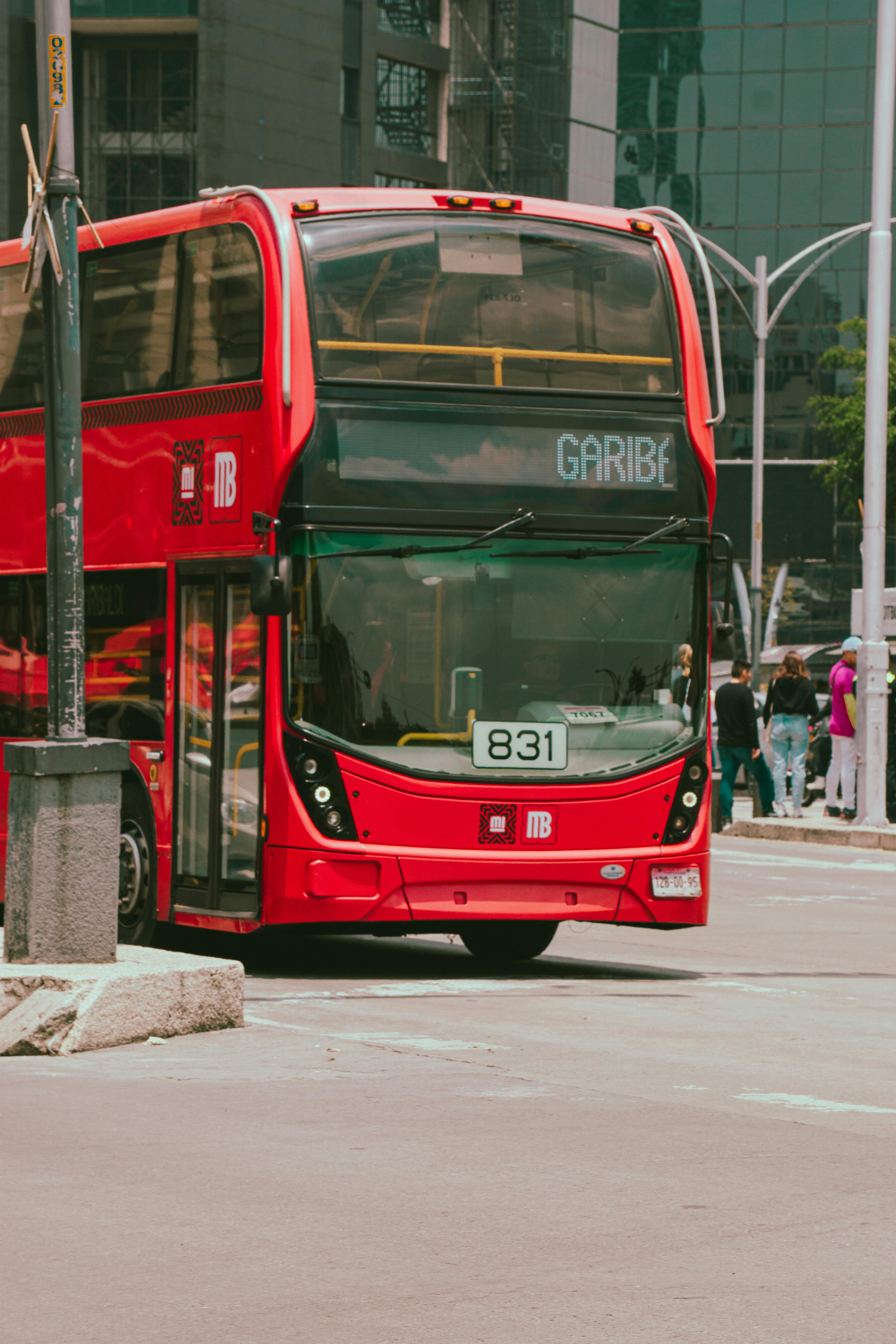 A vibrant red double-decker bus driving on a lively urban street with people.