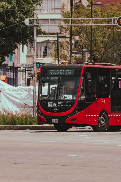 Free A vibrant red electric bus navigating an urban city street during the day. Stock Photo