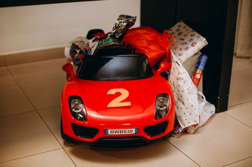 Free Red toy car with number two surrounded by colorful wrapping papers on the floor indoors. Stock Photo