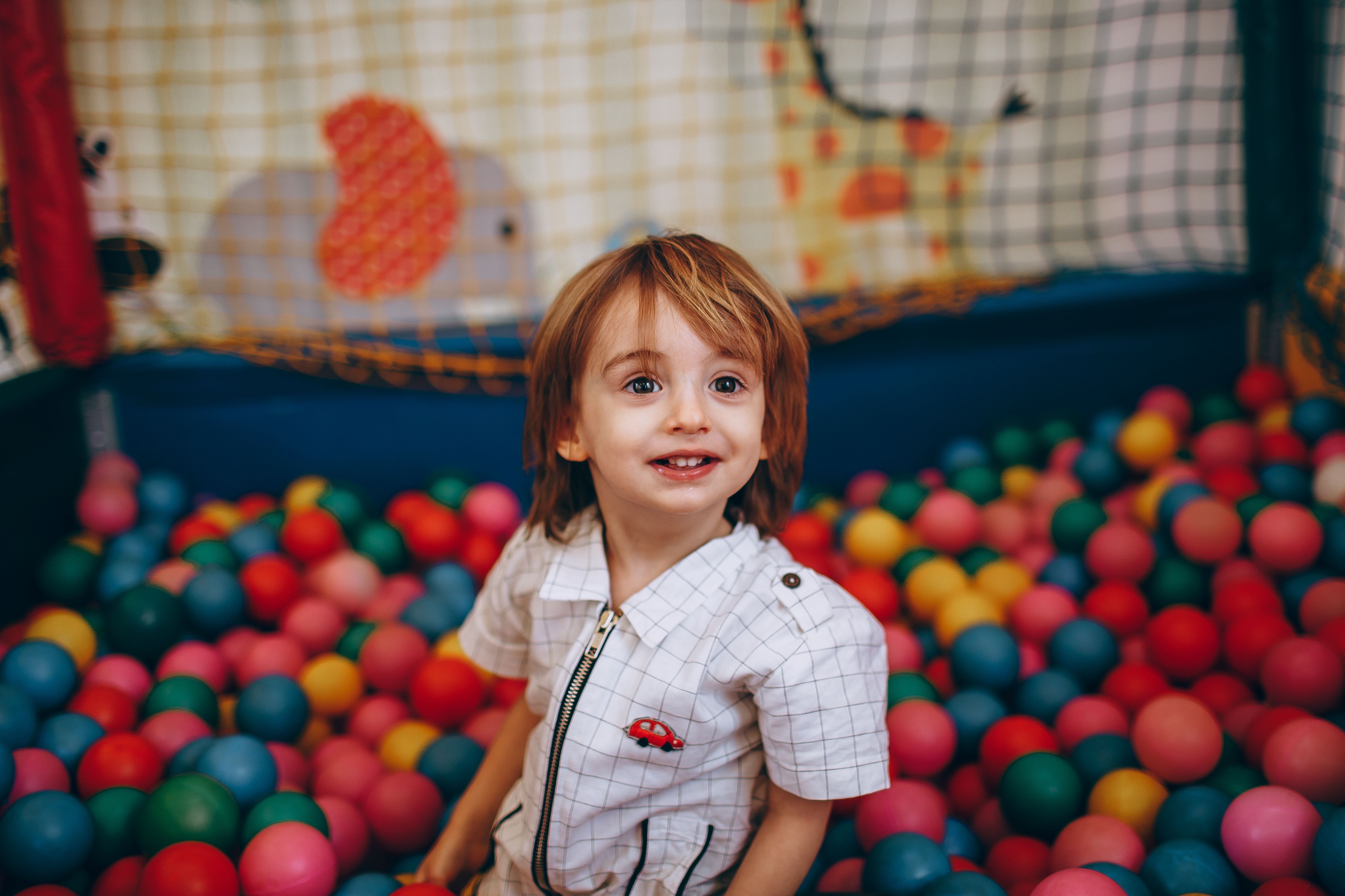 A cheerful child enjoying playtime in a colorful ball pit indoors.