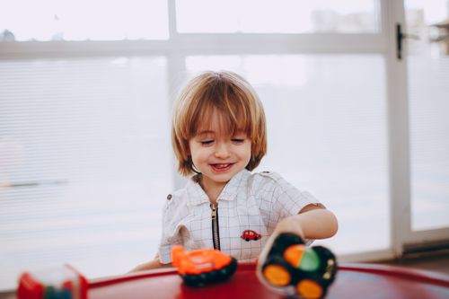 Free Joyful child playing with toy cars by a window, displaying happiness and creativity. Stock Photo
