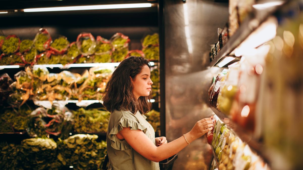 Mulher escolhendo produtos em prateleira de supermercado com atenção