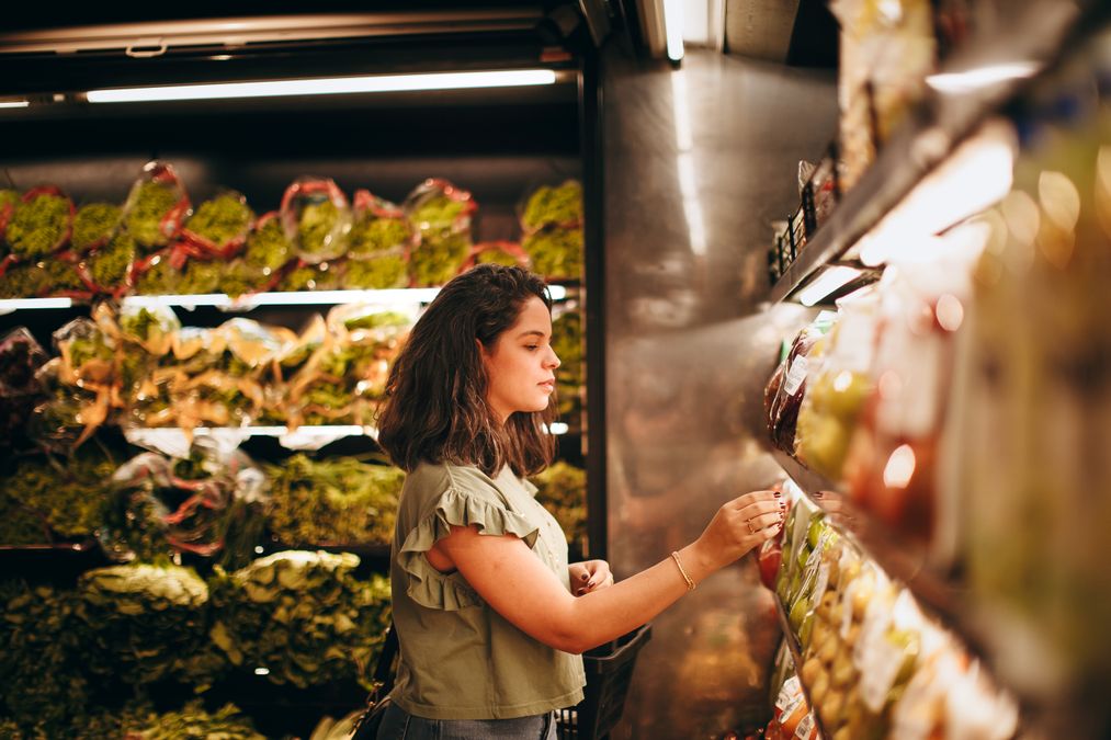 Mulher escolhendo produtos em prateleira de supermercado com atenção