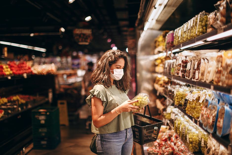 A woman wearing a mask shops for fresh fruits in a grocery store aisle.