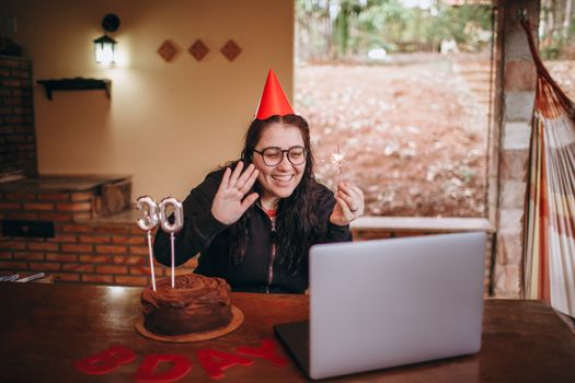 Woman celebrating 30th birthday with a virtual party, cake, and candles.