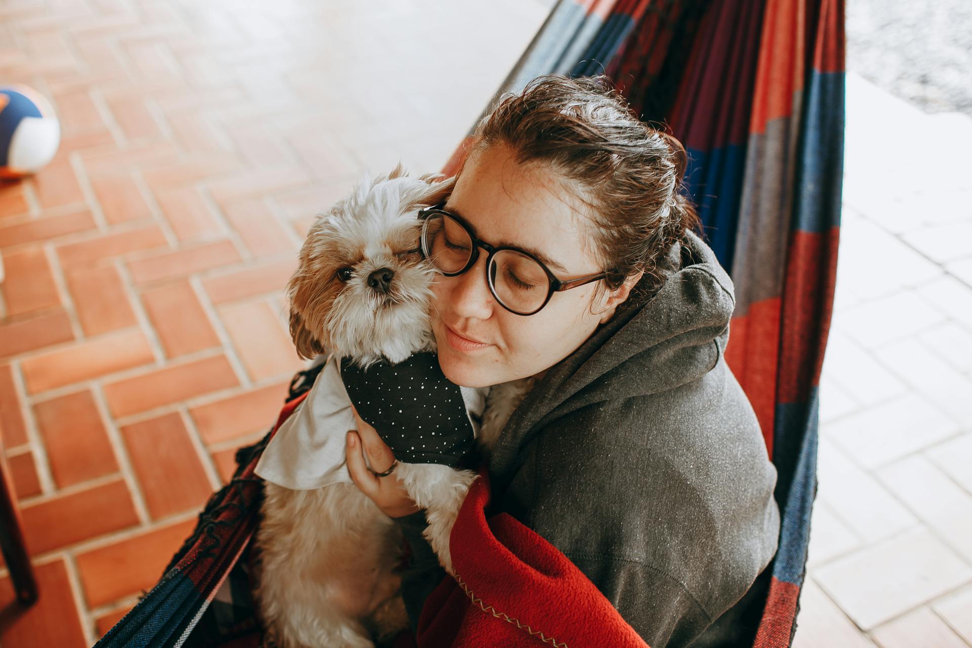 A woman in glasses holding a dog in a hammock