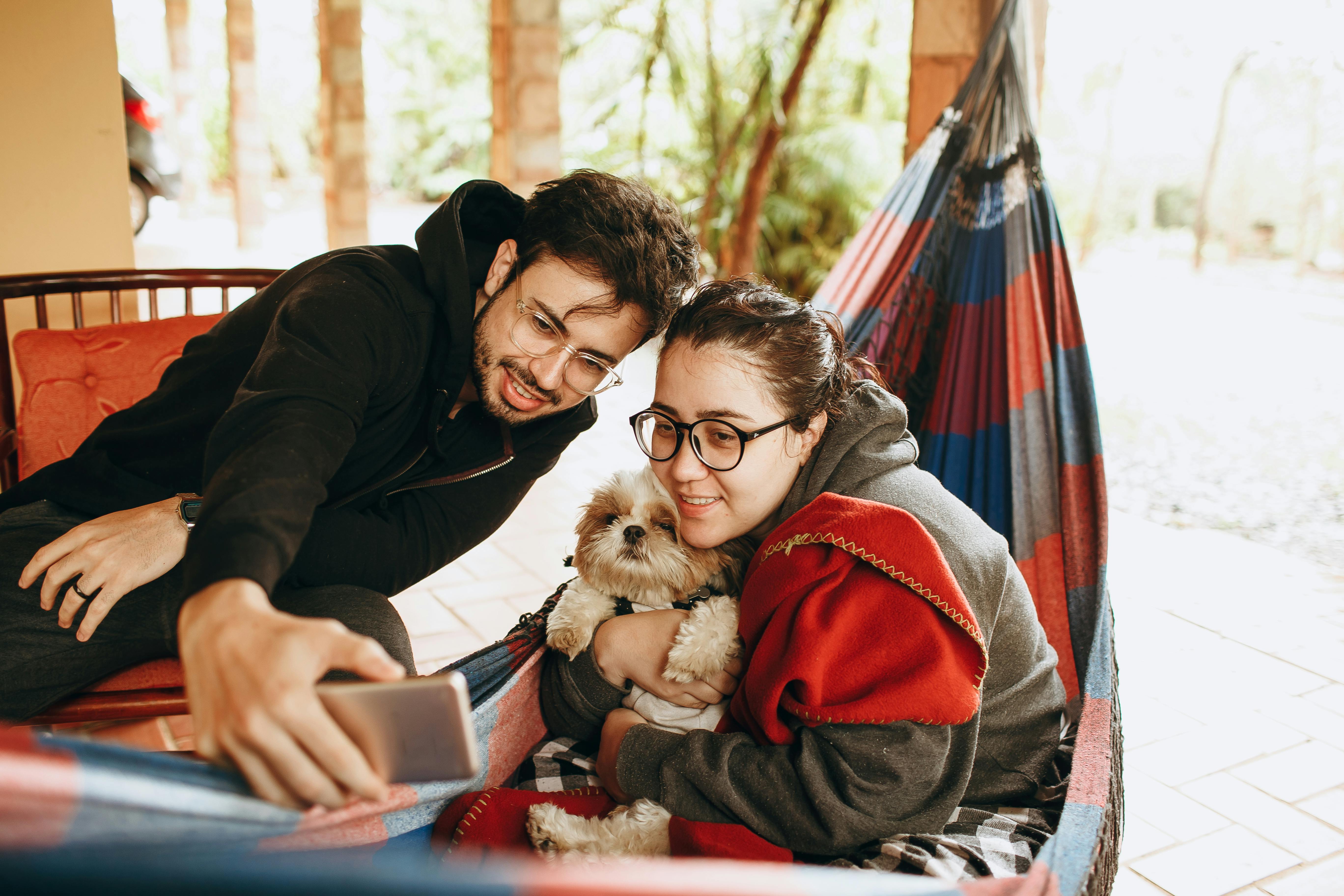 A man and woman sitting in a hammock with a dog