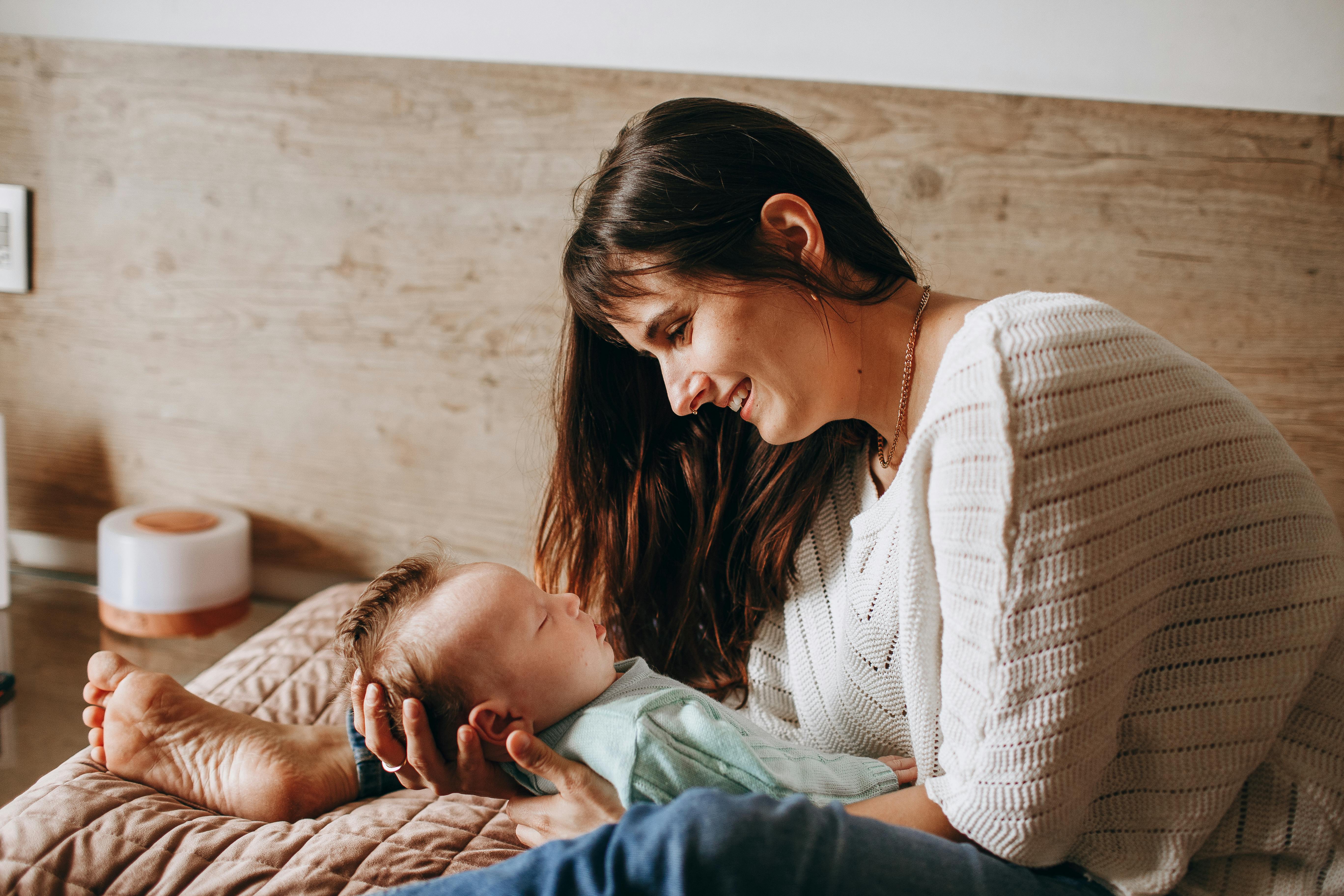 A mother lovingly gazes at her baby in a warm and cozy bedroom, showcasing tender family bonds.