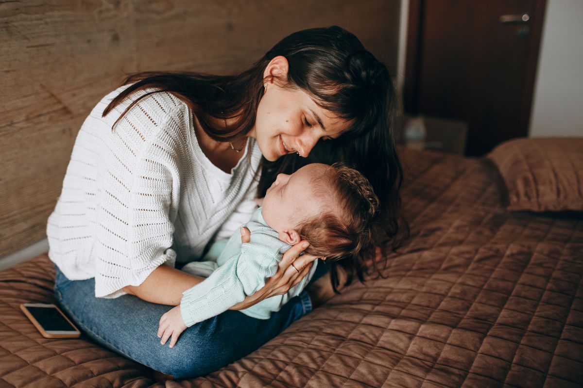 Mother smiling while holding her sleeping newborn on a bed