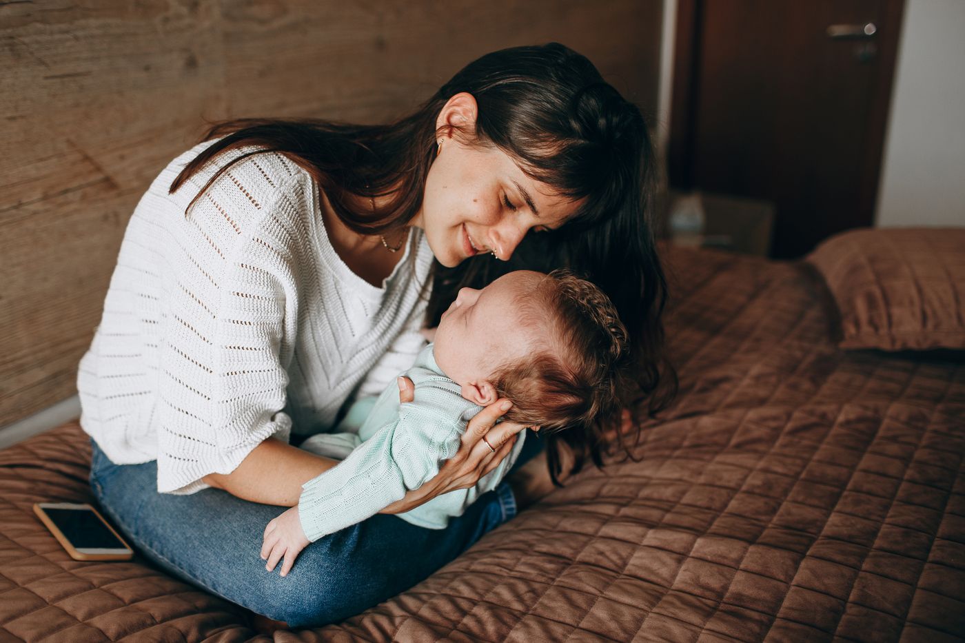 Seated mother looking down at her baby held in her arms indoors