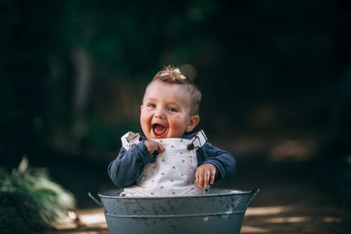 Free Charming portrait of a baby joyfully playing in a metal bucket on a sunny outdoor day. Stock Photo