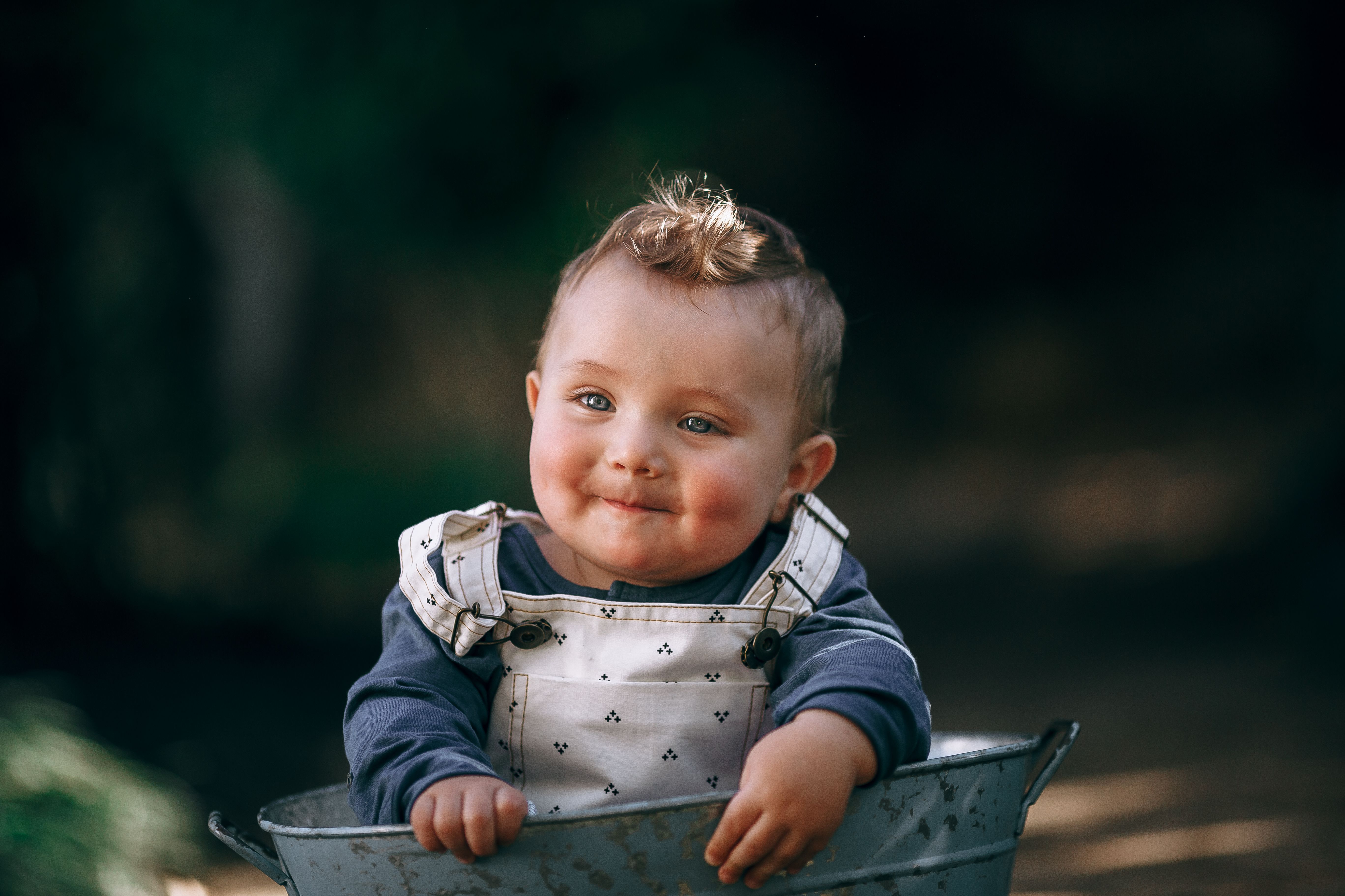 Adorable baby with happy expression in nature, wearing overalls.