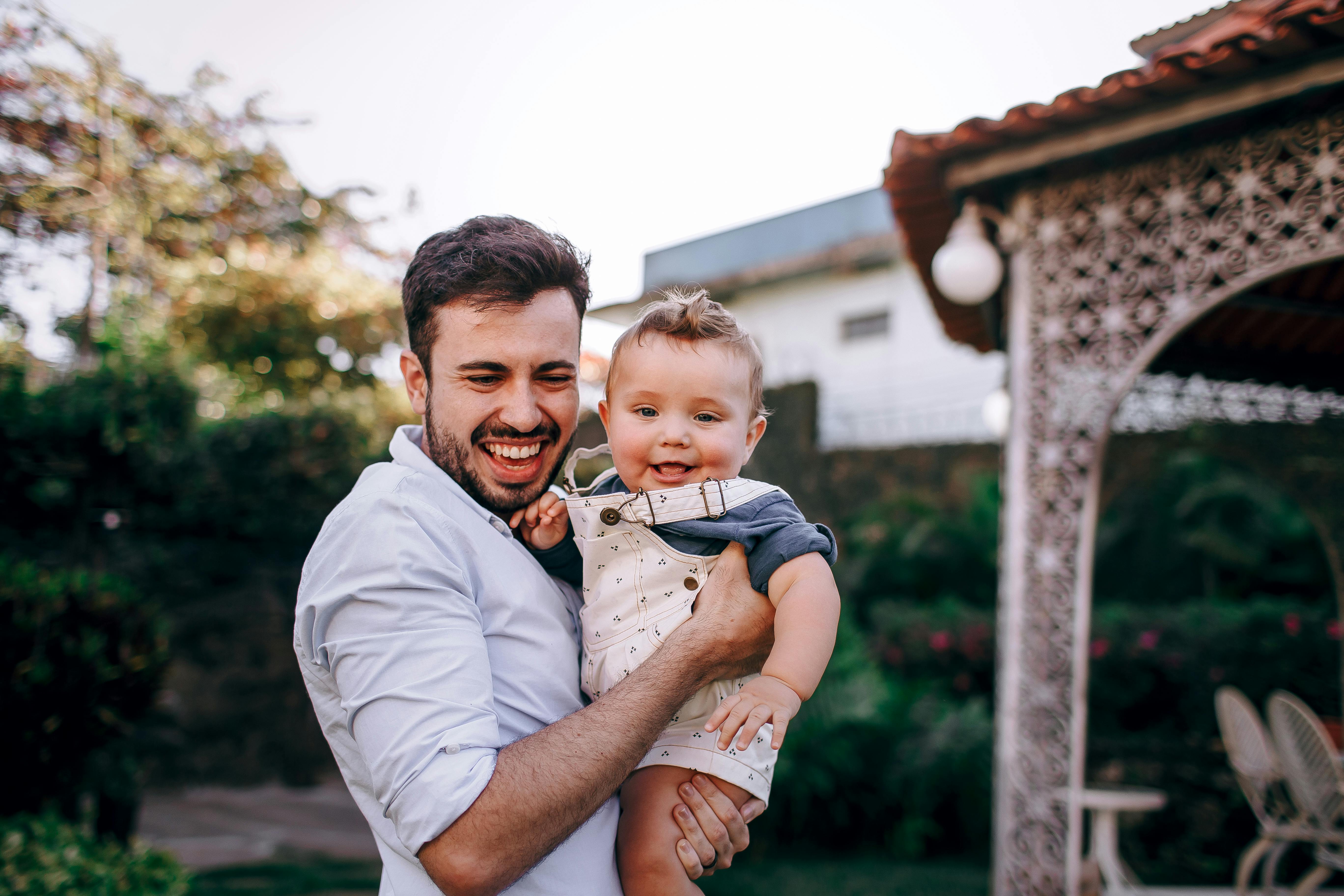 Happy father holding his baby in a sunny outdoor setting, capturing a joyful moment.