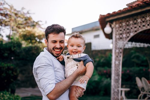 Free Happy father holding his baby in a sunny outdoor setting, capturing a joyful moment. Stock Photo