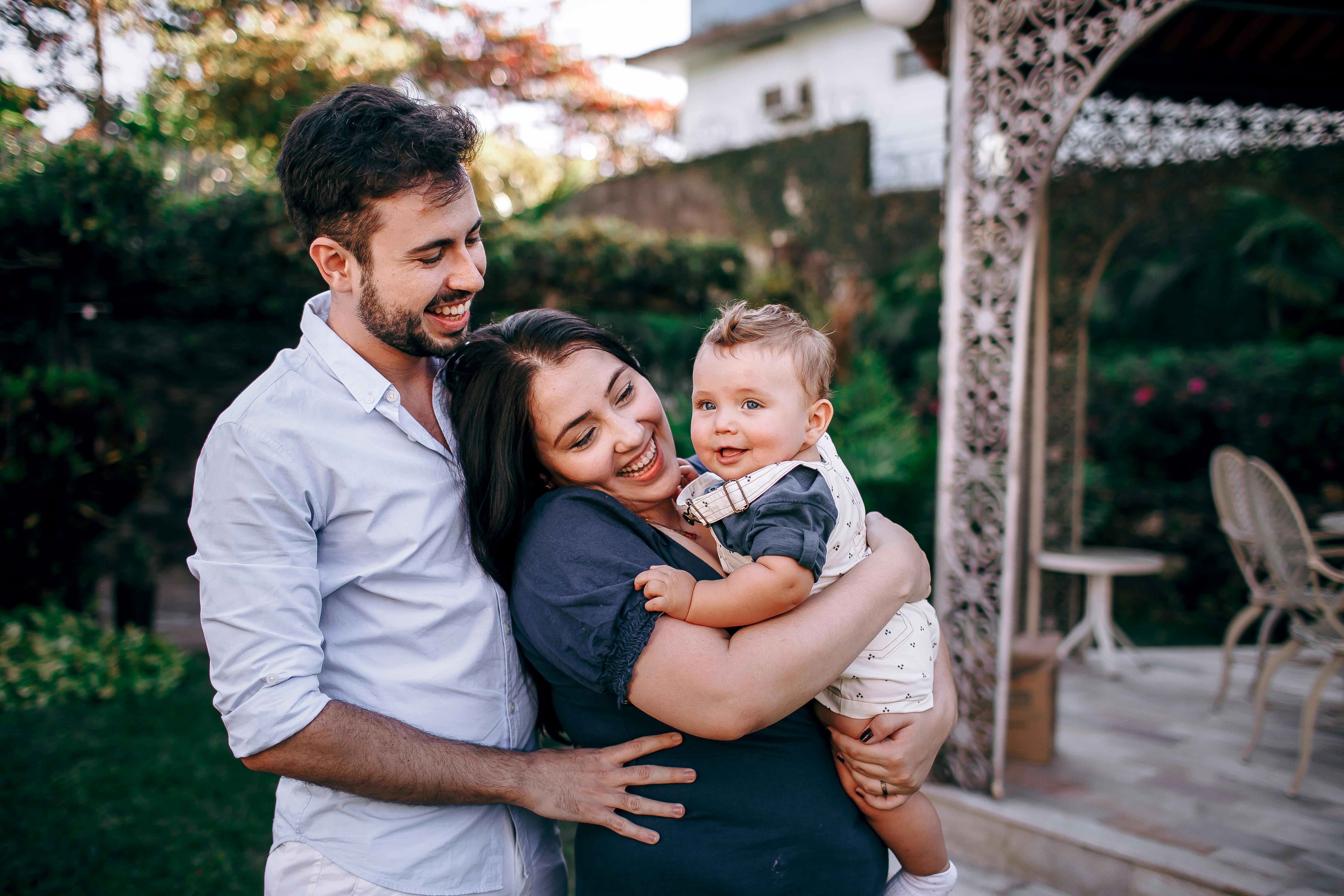 A joyful family moment outdoors with parents and baby in a garden setting.