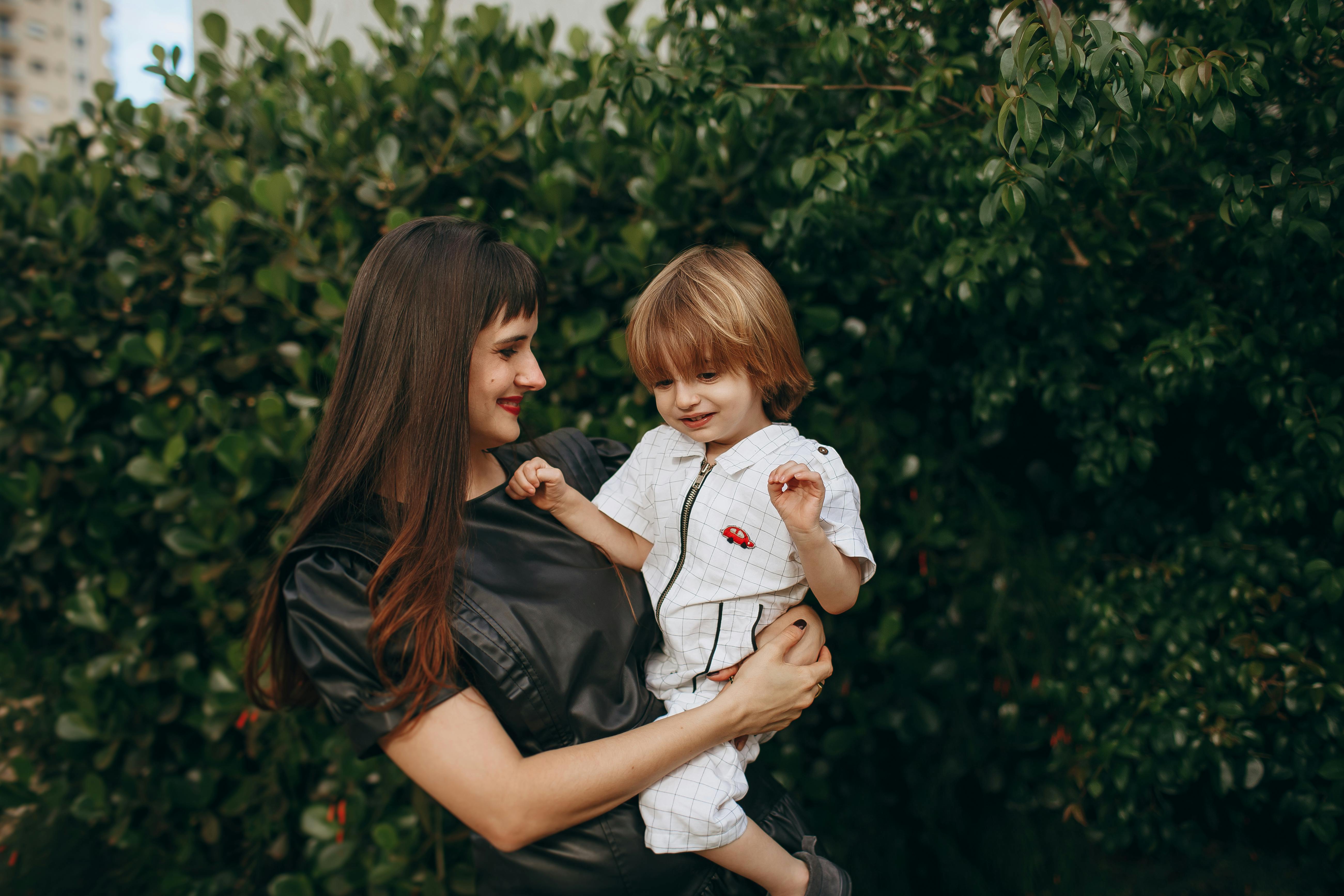 A joyful mother holding her child in a lush green outdoor setting.
