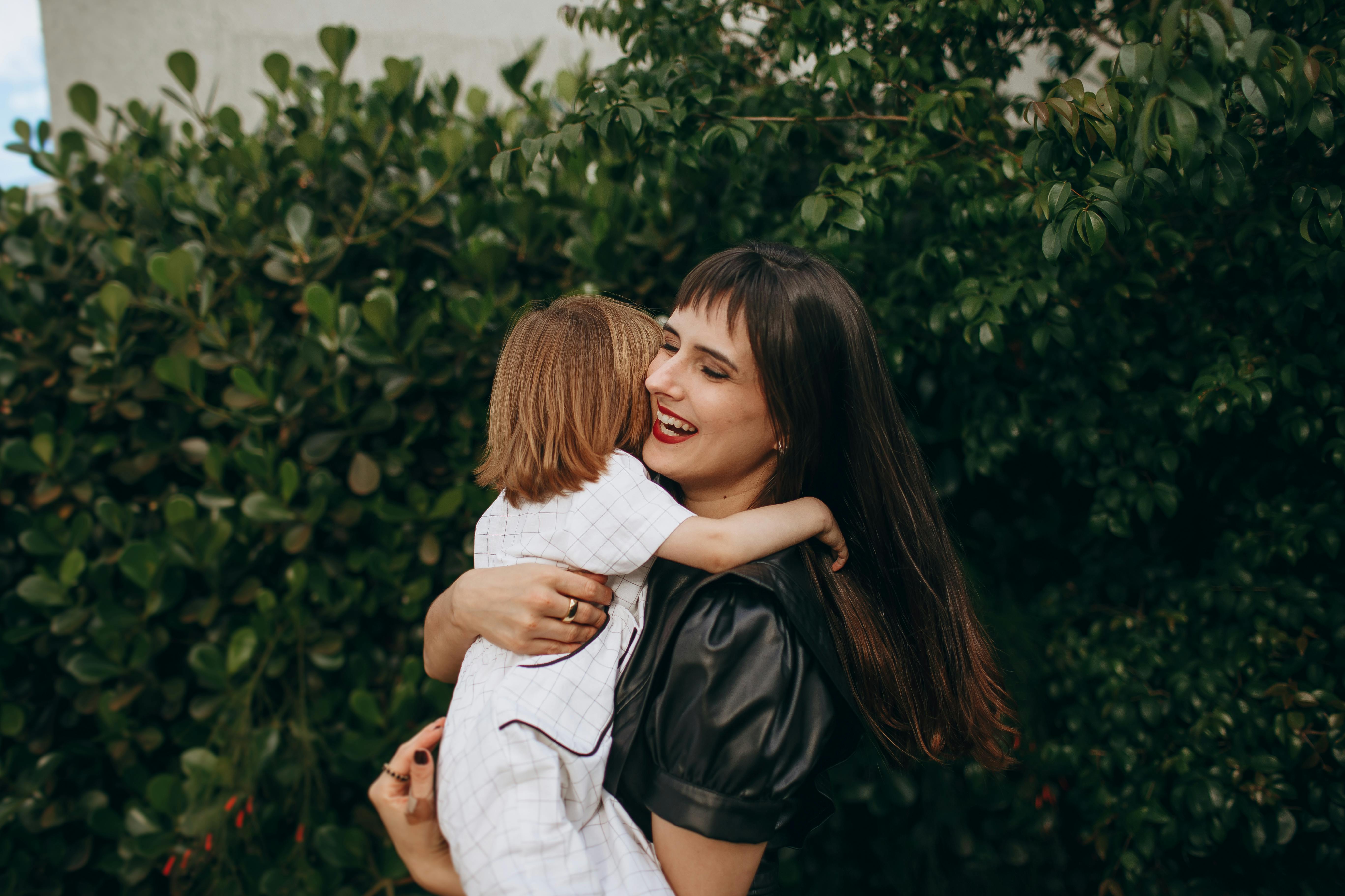 A joyful embrace between a mother and child surrounded by lush greenery.