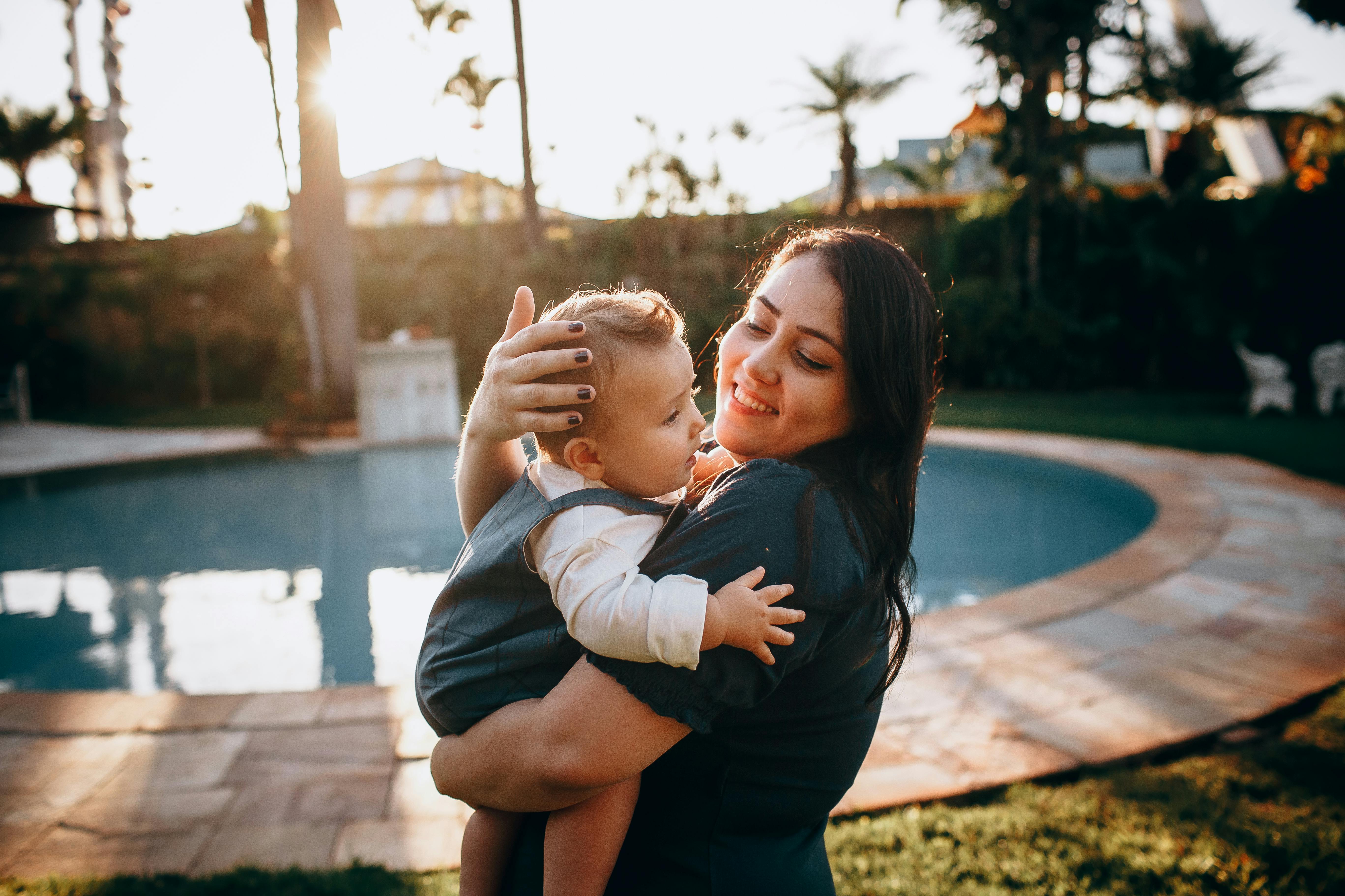 Joyful mother holding her young child by the pool during a sunset, capturing a serene moment.