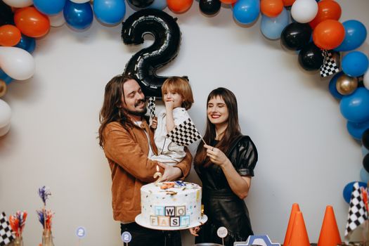 Happy family celebrating a child's second birthday with balloons, cake, and decorations.
