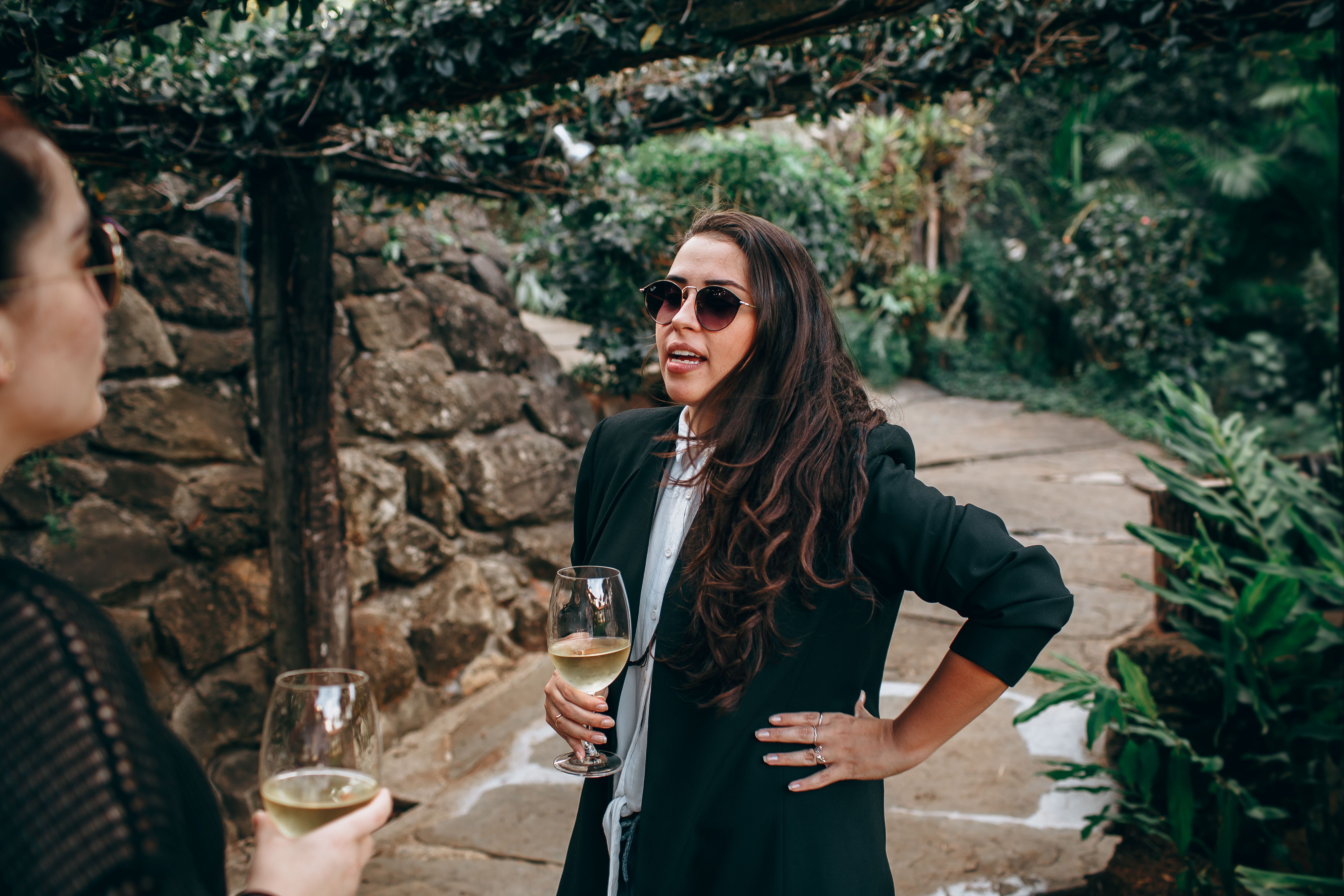 Two women enjoying wine and conversation in a lush outdoor setting.