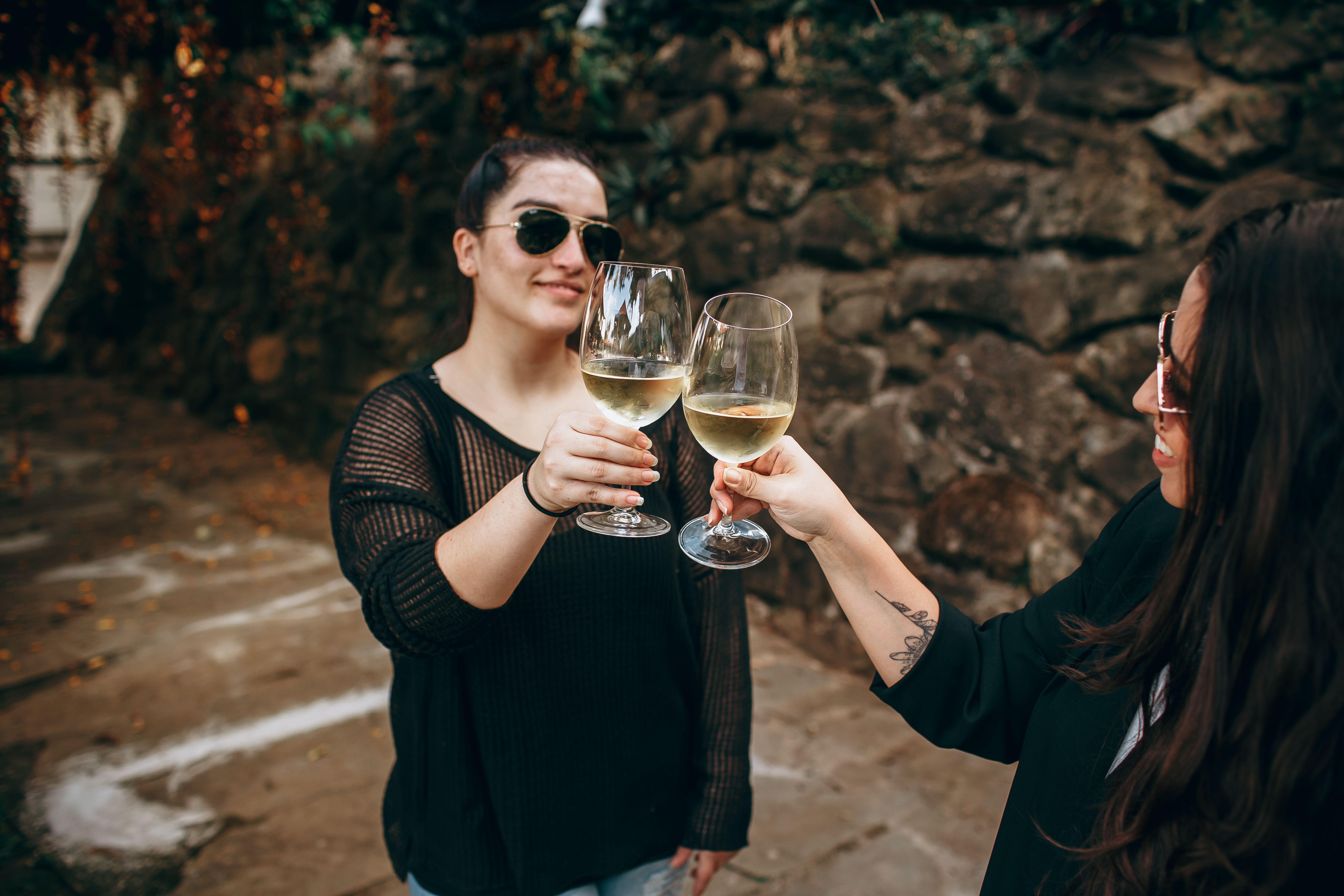 Two women enjoying a moment of celebration with white wine in an outdoor setting.