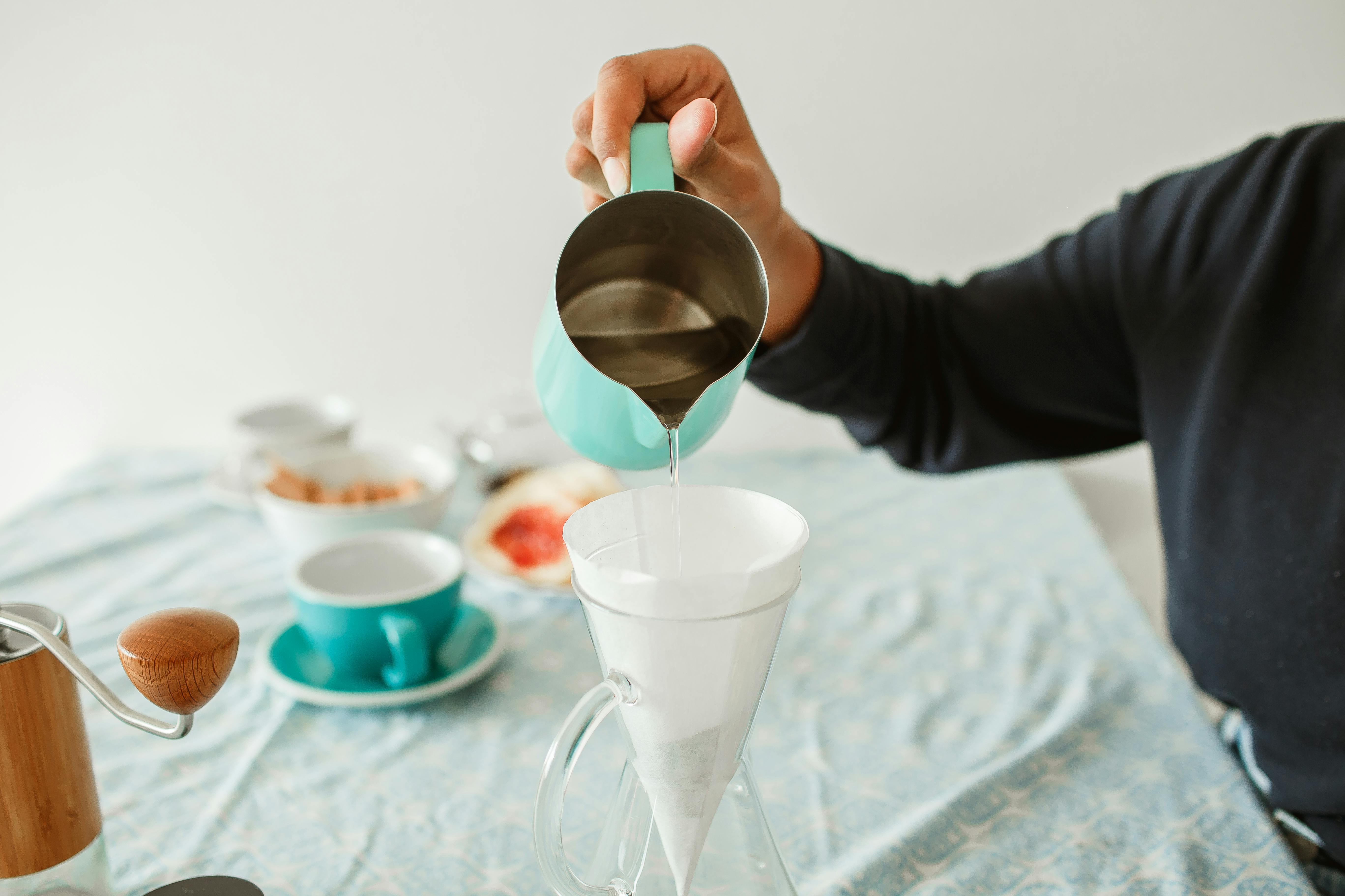 Close-up of a person making coffee with a teal pour over filter and coffee grinder.