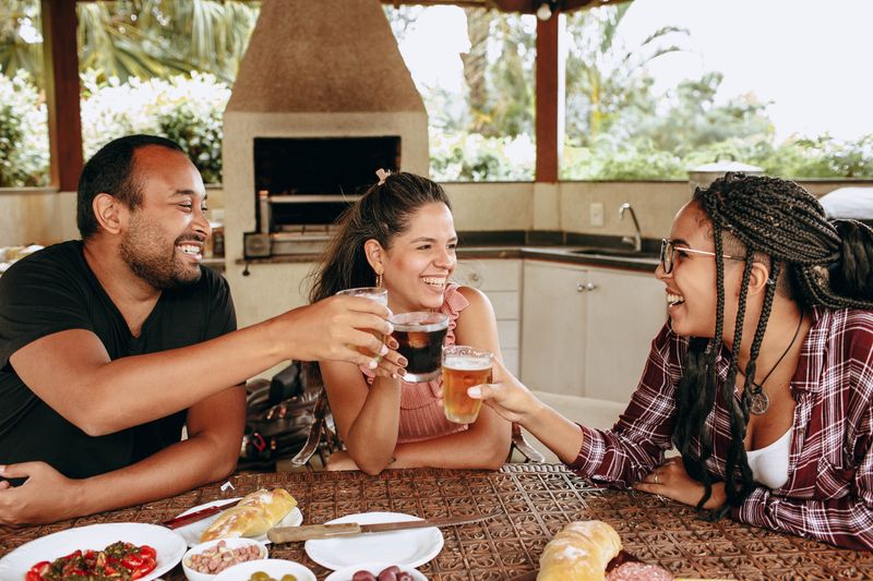 Three friends enjoying food and drinks at an outdoor kitchen table