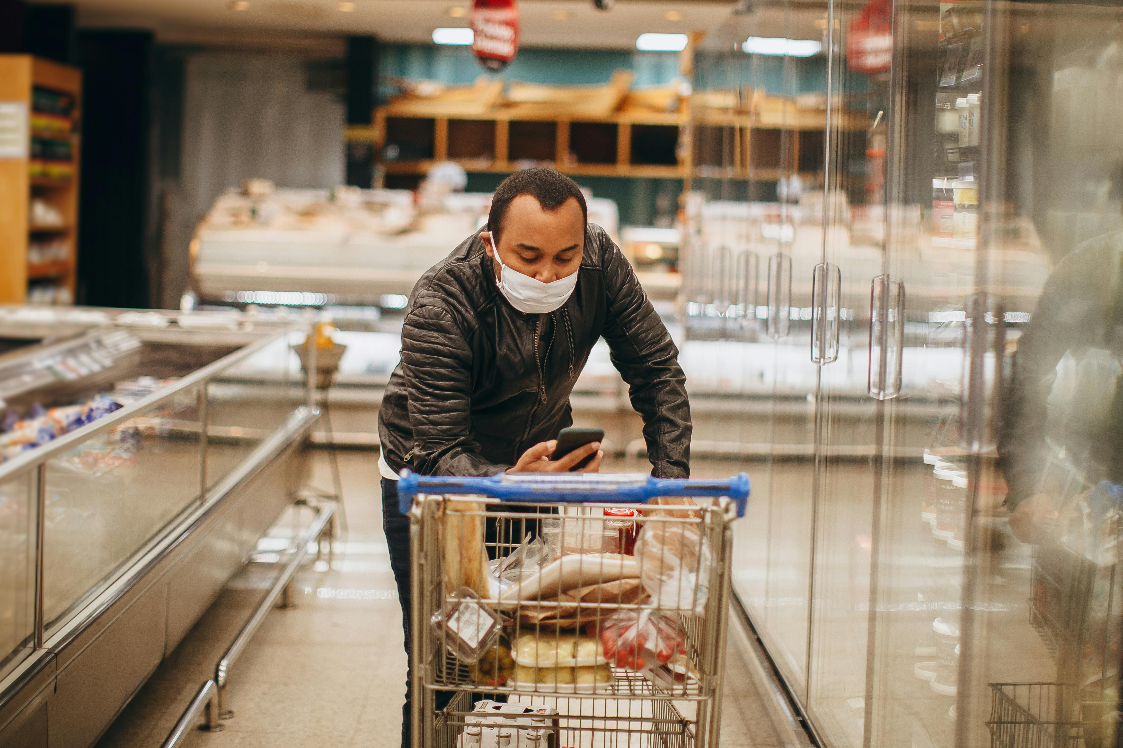 Man wearing mask shops in a supermarket, pushing a cart in the aisle.