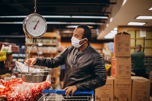 A man weighing produce while wearing a mask in a grocery store, emphasizing shopping safety.