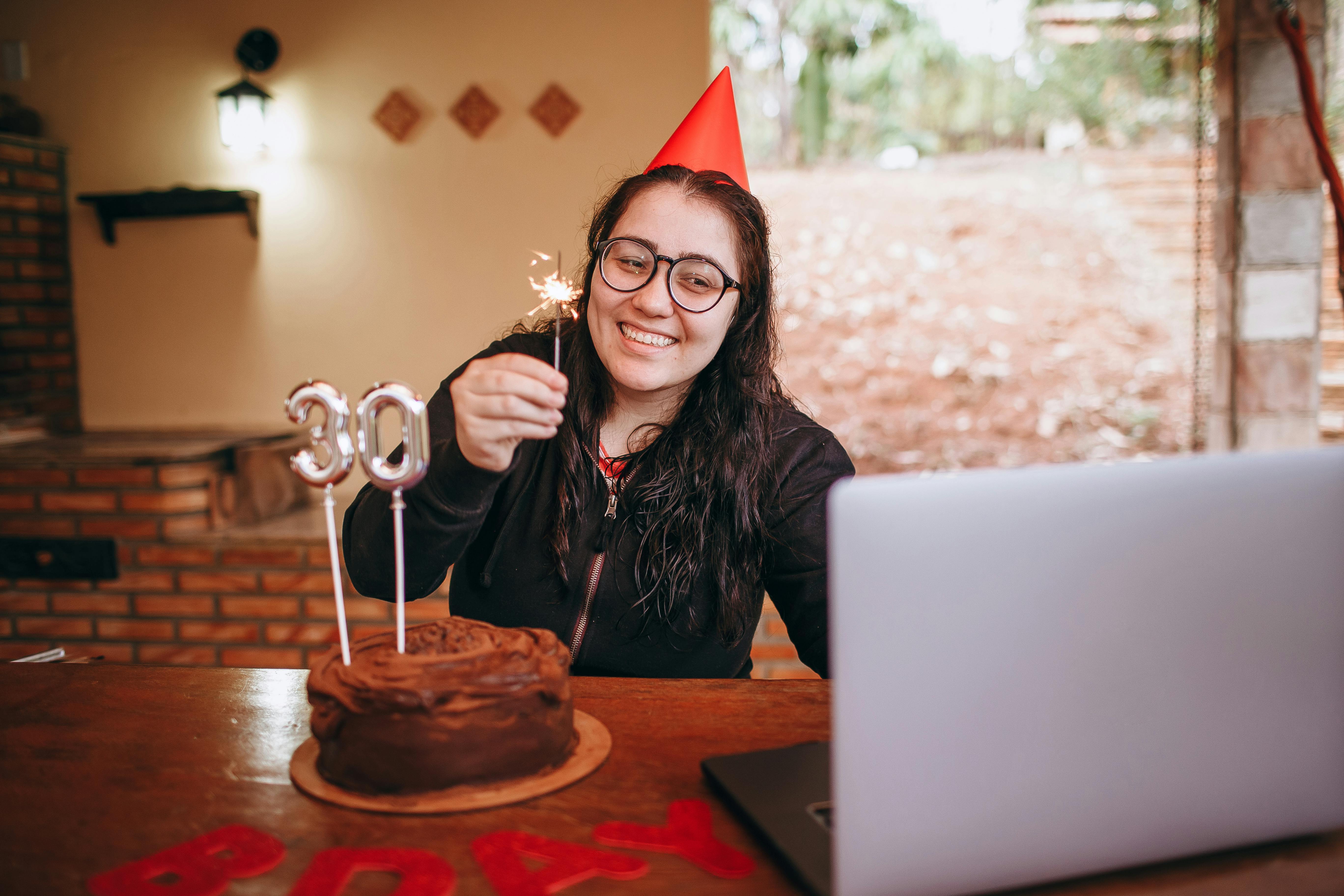 smiling woman with birthday cake in front of laptop