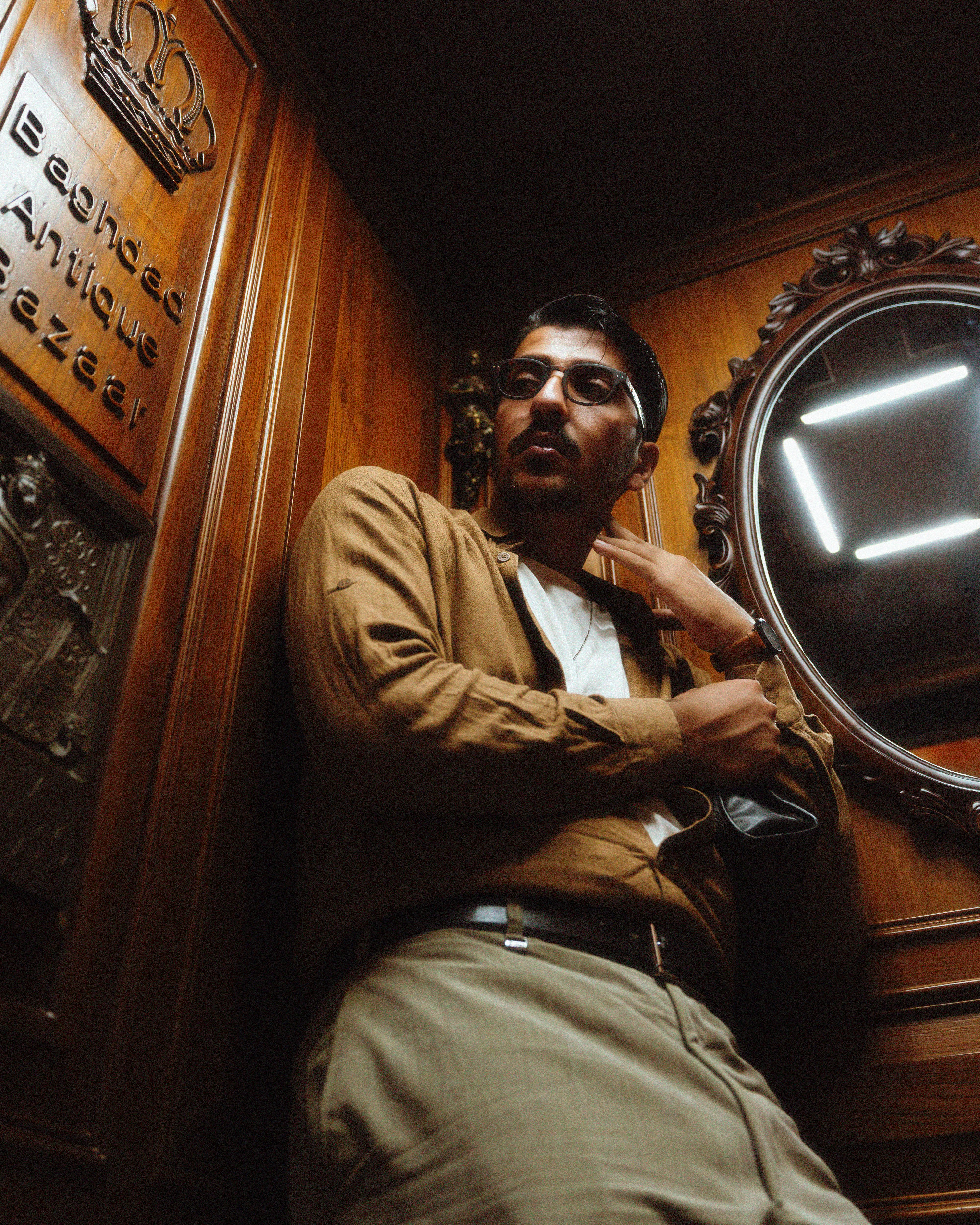 Portrait of a fashionable man posing indoors at a vintage setting with a mirror and wood paneling.