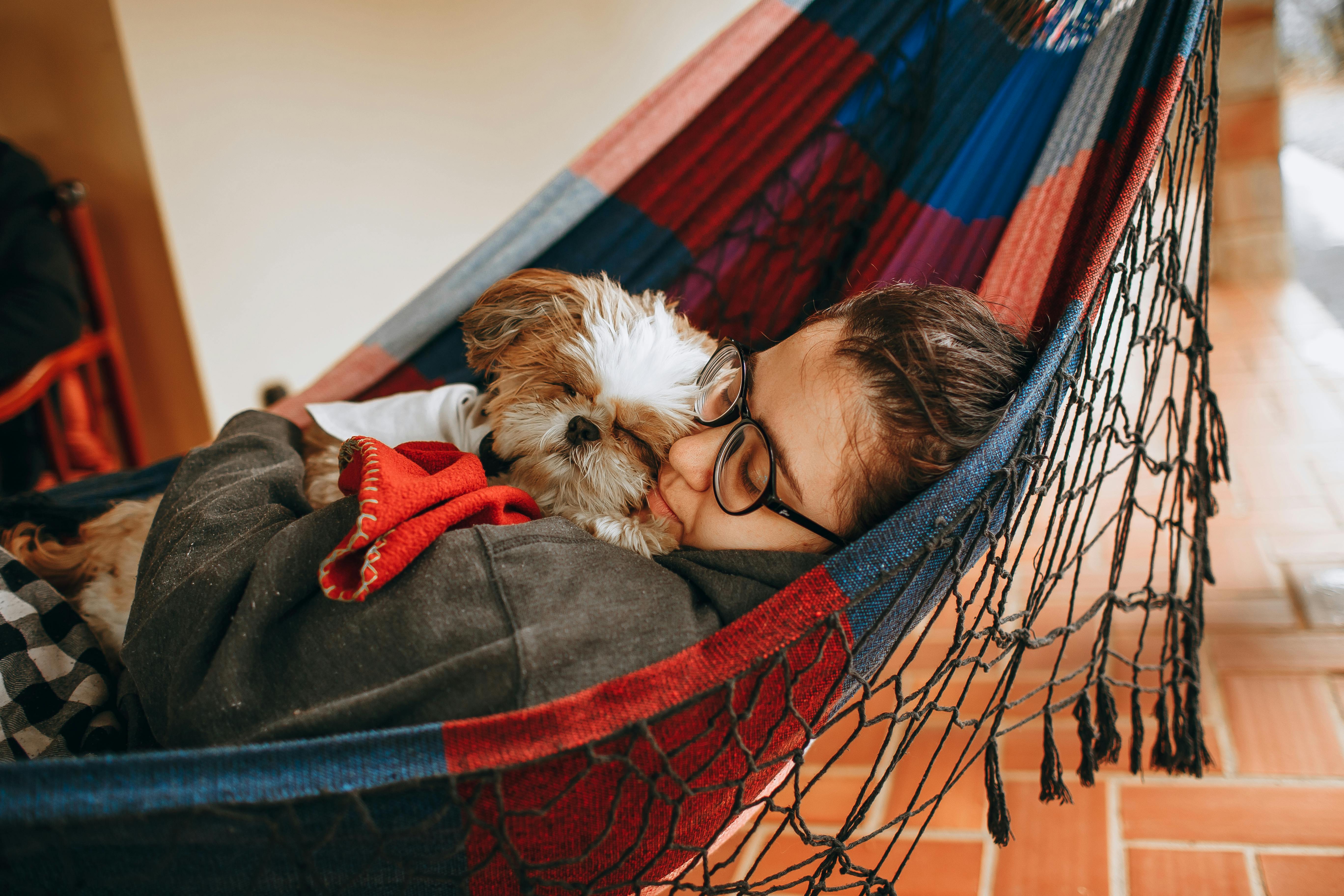 A woman is laying in a hammock with her dog